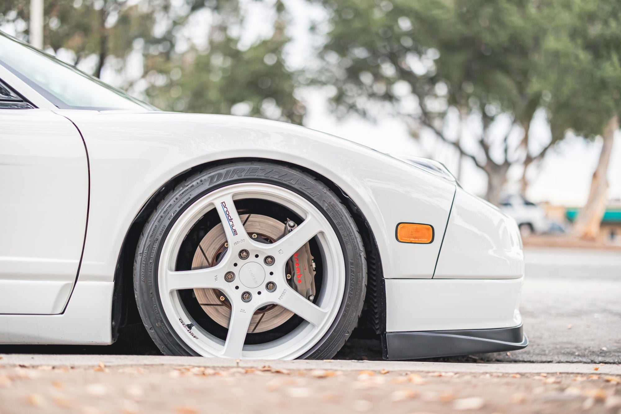 Close up of white prodrive GC-05 wheels on white NA2 NSX with Brembo brake calipers parked on street.